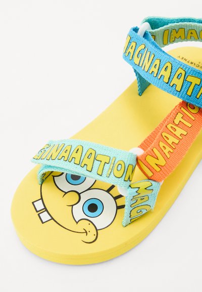 Geel sandaal met een SpongeBob ontwerp, blauwe en oranje gestructureerde bandjes met de tekst "IMAGINATION" en een gladde rubberen zool.