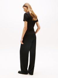 T-shirt noir ajusté, à manches courtes, associé à un pantalon noir à jambes larges. Texture simple, design minimaliste, porté avec des chaussures noires.