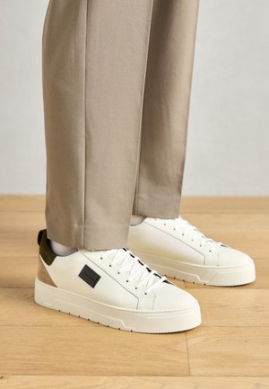 Sneakers bianchi in pelle con un pannello laterale texturizzato in verde oliva e beige. Presentano una patch con logo nera e una suola texturizzata con un design elegante.