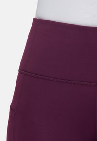 Bordowe legginsy z wysokim stanem wykonane z elastycznego materiału, charakteryzujące się gładką powierzchnią i wzmocnionymi szwami wzdłuż pasa i boków.