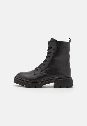 Black ankle boots made of leather, featuring a round toe, lace-up front, cushioned collar, and chunky rubber sole with traction patterns.