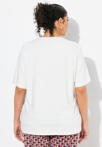 T-shirt blanco de manga corta hecho de una tela suave, con un corte relajado y un cuello redondo clásico. La vista trasera muestra una textura lisa.