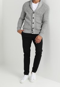 Grå ribbade koftor med sjalkrage och framfickor, i kombination med svarta åtsittande byxor och vita sneakers. Knapparna är mörkbruna.