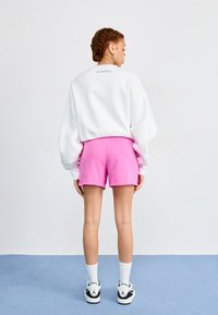 Vit oversized sweatshirt med en baketikett, kombinerad med rosa shorts och vita strumpor. Svarta och vita sneakers fulländar looken.