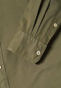 Manga de camisa verde oliva con cierre de botón, diseño plisado y textura de tela suave y ligera.