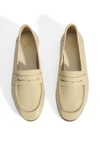 Beige leren loafers met een gestructureerde afwerking, voorzien van een subtiele stiknaad en een merkplaatje in de zool, ontworpen voor comfort.