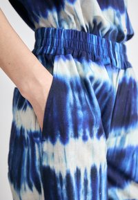Combinaison en tie-dye bleu et blanc avec taille élastique et poches latérales, affichant une coupe décontractée et une texture de tissu douce.