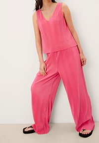 Top sin mangas de canalé rosa con escote en V, combinado con pantalones de pierna ancha, ambos en una tela ligera, creando una silueta relajada.