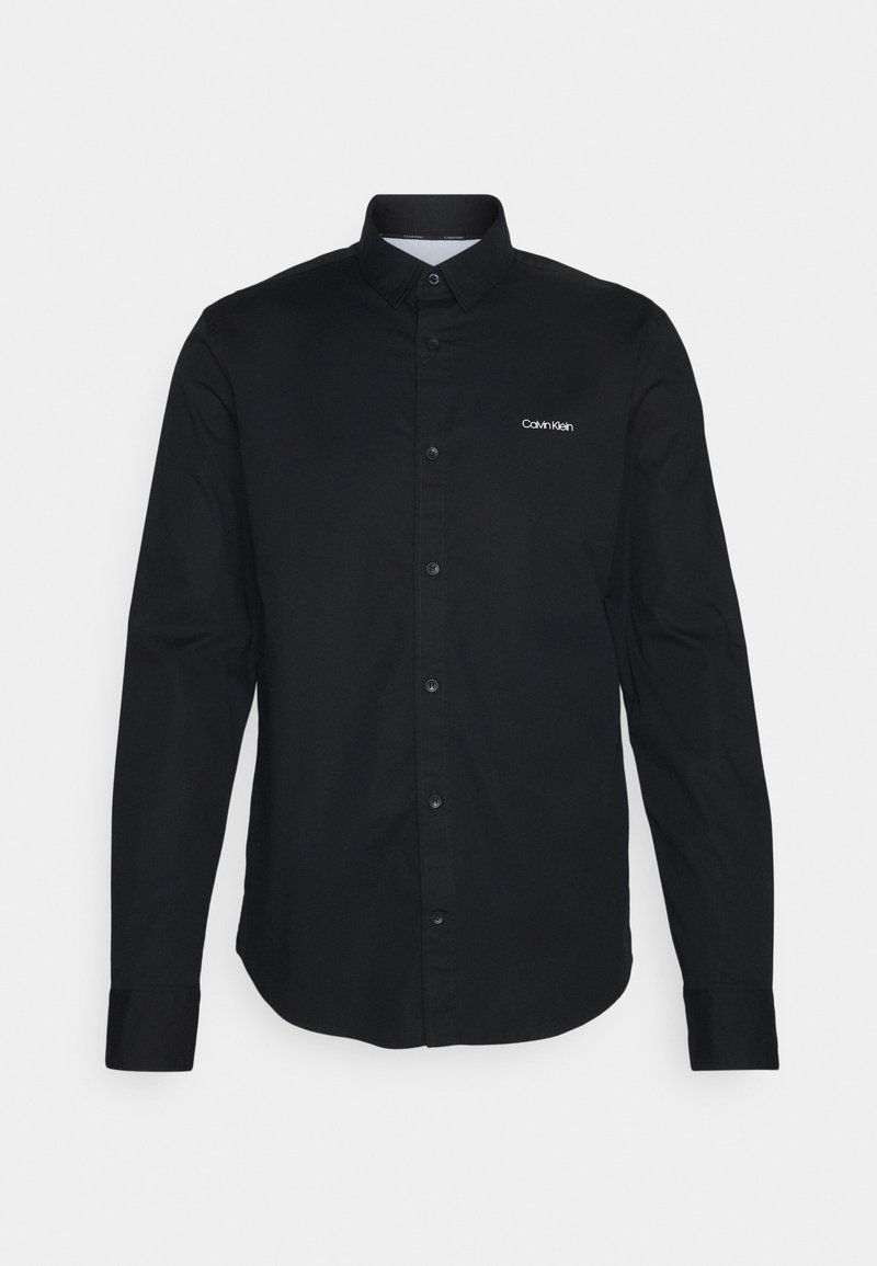 Chemise noire à manches longues avec col et petits boutons, logo blanc "Calvin Klein" sur le côté gauche de la poitrine.