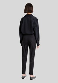 Camicia nera oversize con un logo discreto sul retro, pantaloni neri slim e scarpe piatte con motivo. Tessuto liscio con vestibilità rilassata.