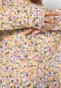 Bloemenprint lange mouwen jurk met een geplooid ontwerp in tinten geel, paars en groen, gemaakt van een lichtgewicht, gestructureerde stof.