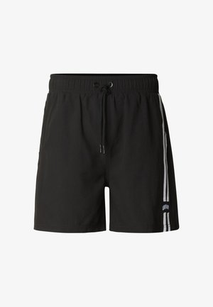 Czarne sportowe spodenki z elastycznym paskiem, sznurkiem do ściągania oraz dwoma białymi pionowymi paskami po prawej stronie przy krawędzi z napisem "UNFAIR".