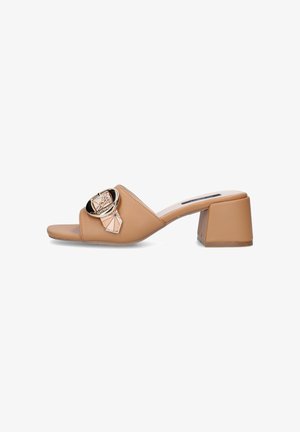 Mule beige con punta aperta, tacco a blocco e grande fibbia decorativa dorata sulla larga fascia trasversale.