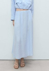 Himmelblaue Leinen-Langskirt mit Falten, kombiniert mit einer passenden, kurzen Bluse und nude-farbenen Riemchensandalen. Glatte Textur, schlichtes Design.