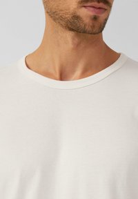 Mann mit hellbeard, der ein einfaches weißes Rundhalsausschnitt-T-Shirt trägt, Nahaufnahme des Nackens und unteren Gesichts.