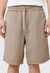 Beige shorts tillverkade av lättviktigt tyg, med elastisk midja, dragsko och sidofickor. Slät textur och avslappnad passform.