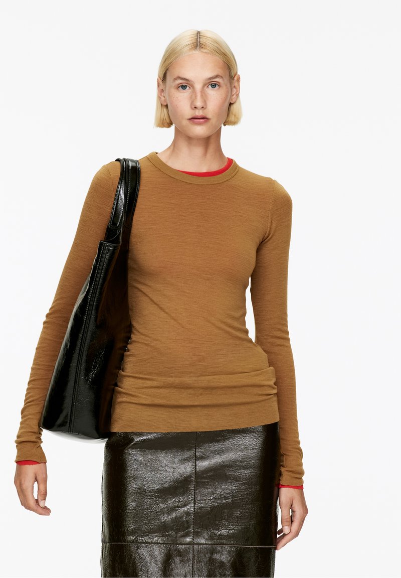 Chemise marron à manches longues avec un col rond rouge, associée à une jupe noire en cuir brillante et un grand sac cabas noir. Texture lisse dans l'ensemble.