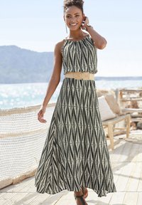 Maxi dress featuring a black and white leaf pattern, halter neckline, and a wide beige belt. Flowing fabric with a smooth texture.