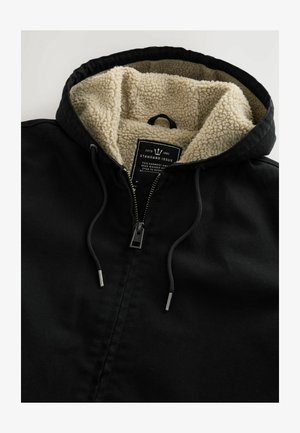 Mustapintainen vetoketjullinen takki, jossa on kermaisen värinen, teksturoitu fleecevuori. Varustettu nyörikiinnitteisellä hupulla ja sisällä hoito-ohjeita sisältävällä tarralla.