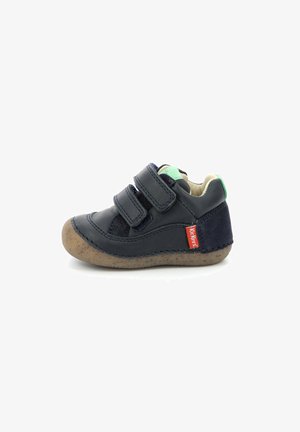 Zapato de cuero marino para niño pequeño con dos correas de Velcro, acento verde en el talón y suela marrón texturizada. Detalles de costura destacados.