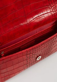 Borsa in pelle rossa con effetto coccodrillo e finitura lucida, dotata di chiusura a scatto in argento e tasca interna con zip.