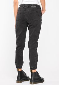 Černé džínové teplákové kalhoty se zúženými kotníky, pěti kapsami a štítkem na pasu. Nošeny s černými šněrovacími botami s masivní podrážkou.