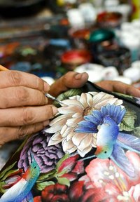 Handgeschilderd bloemmotief met levendige kleuren op een oppervlak; bevat een mix van bloemen en een kolibrie, met inkijk in gedetailleerd vakmanschap.