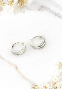 Silverörhängen i form av hoops med tre texturerade, graderade band. Tillverkade av glänsande metall, med en slät yta och böjd design.