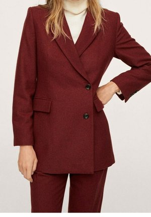 Blazer in lana bordeaux con vestibilità sartoriale, monopetto, revers a punta e tasche laterali. Accompagnato da un dolcevita beige.