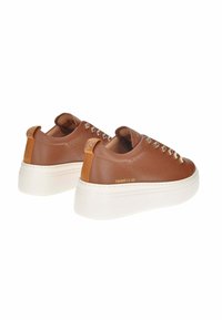 Sneaker slip-on in pelle marrone testurizzata con borchie metalliche, suola spessa bianca e linguette posteriori in contrasto color tan. Nome del marchio visibile sul lato.