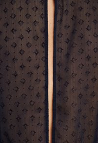 Tissu noir transparent avec de petits motifs en losange et une ouverture verticale centrale révélant la peau en dessous.