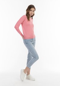 Rózsaszín, hosszú ujjú pulóver, bordás mandzsettákkal és aljjal, világoskék, slim-fit farmernadrággal és fehér sportcipőkkel viselve. Egyszerű, laza öltözet.