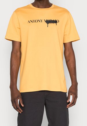 Gelbes Baumwoll-T-Shirt mit Rundhalsausschnitt. Mit schwarzem "ANTONY MORATO"-Text und einem tropfenden Farbmuster. Kurzärmlig, lässige Passform.