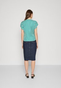 Kortermet bluse i teal og hvite striper, kombinert med en mørk denim blyantskjørt, som har en ufinsket kant og baklommer.