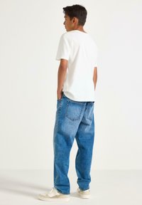 Hvid T-shirt parret med lyseblå, løstsiddende denimjeans. Jeansene har en falmet tekstur og to baglommer. Båret med lyse sneakers.