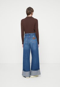 Vaqueros de pierna ancha con un lavado claro, que presentan un puño de contraste y una blusa de manga larga acanalada en marrón. Se muestra la vista trasera.