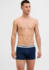 Tumši zili bokseršorti, izgatavoti no mīksta auduma ar pieguļošu dizainu, ar baltu jostu, uz kuras melnā krāsā ir drukāts "JACK & JONES".