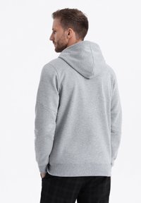 Sweat à capuche gris avec une coupe décontractée, présentant des poignets et un ourlet côtelés. Texture lisse avec un design simple et épuré.