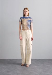 Grafisk t-skjorte med abstrakte blå og beige mønstre, kombinert med kremfargede fleece cargo-bukser med sidelommer.