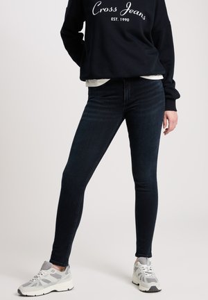 Dark blue skinny jeans in denim, featuring a high waist and slight fading. Paired with a black sweatshirt and grey sneakers.