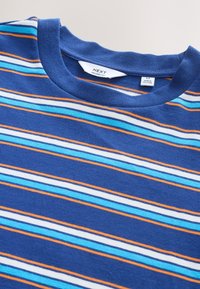 Blå bomuld T-shirt med vandrette striber i lyseblå, hvid og orange. Har rund halsudskæring og et mærke, der angiver afslappet pasform.
