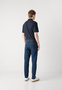 Cămașă polo de culoare bleumarin asortată cu blugi denim albaștri și adidași albi. Blugii au buzunare la spate și o croială modernă, elegantă. Design minimal.