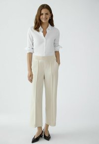 White button-up shirt with rolled sleeves, paired with beige high-waisted pleated trousers and black slingback heels. Smooth fabrics, simple design.