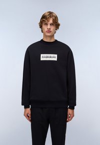 Black sweatshirt with a round neckline, ribbed cuffs, and hem. Features a rectangular white logo label on the front. Soft fabric texture.