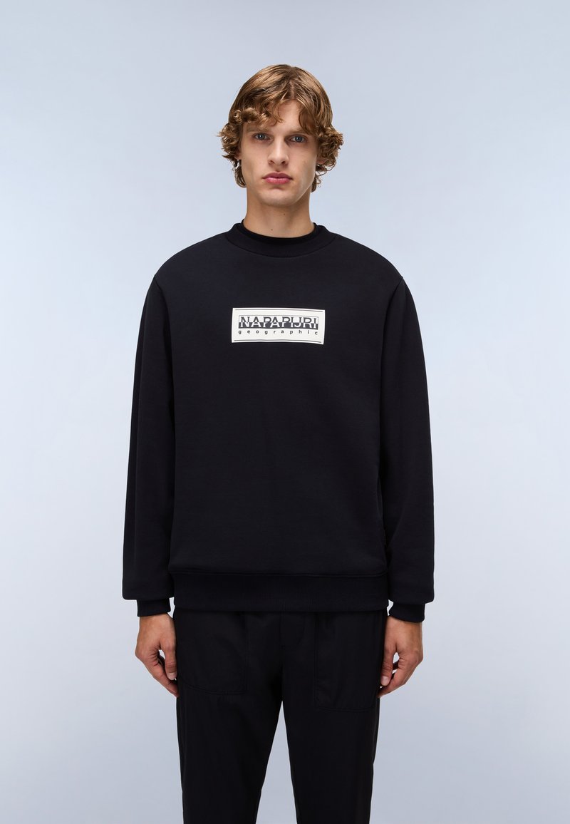 Black sweatshirt with a round neckline, ribbed cuffs, and hem. Features a rectangular white logo label on the front. Soft fabric texture.