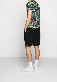 Černá košile s krátkým rukávem s tropickým potiskem, na kterém jsou zelené listy a růžové květy, v kombinaci s černými šortkami. Bílé tenisky a ponožky do kotníku.