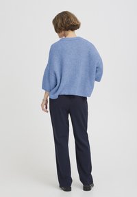 Pull en maille bleu clair avec un col rond et des manches courtes larges, associé à un pantalon droit bleu marine foncé.