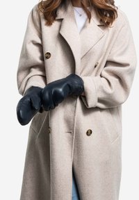 Black leather mittens worn over a light beige wool coat, featuring deep pockets and gold buttons, contrasting textures and colors.