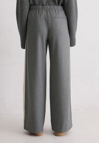 Osoba ubrana w szare szerokie spodnie z elastycznym pasem i jedną tylną kieszenią, w połączeniu z ciemnoszarym swetrem.