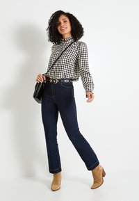 Camisa de cuadros en blanco y negro de manga larga con cuello con volantes, jeans azul oscuro y botas de tobillo con tacón color beige. Incluida bolsa cruzada negra.